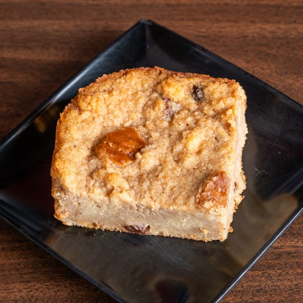 A square slice of golden-brown bread pudding with a crispy top, served on a black plate.