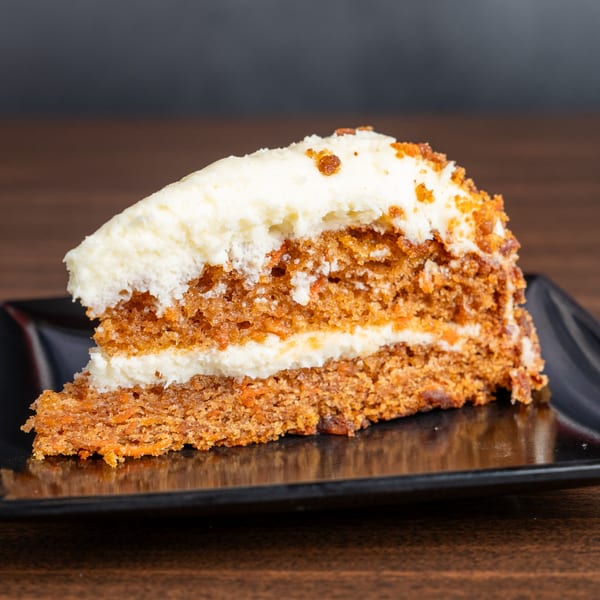 A slice of carrot cake with white cream cheese frosting and crumbs on a black plate.